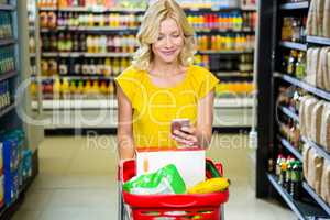 Smiling woman with smartphone pushing trolley in aisle