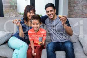 Smiling family eating pizza on the sofa
