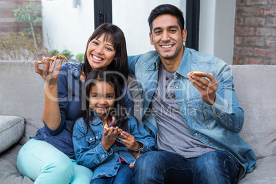 Smiling family eating pizza on the sofa