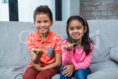 Smiling siblings eating pizza on the sofa