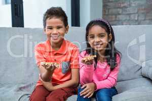 Smiling siblings eating pizza on the sofa