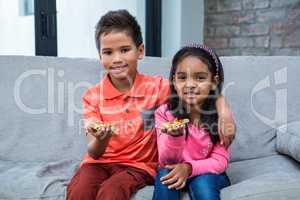 Smiling siblings eating pizza on the sofa