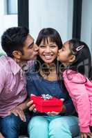 Happy mother being kissed by her children while holding a presen