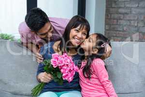 Happy mother holding roses being kissed by her daughter