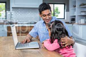 Smiling father using laptop with his daughter