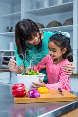 Smiling mother washing salad with her daughter