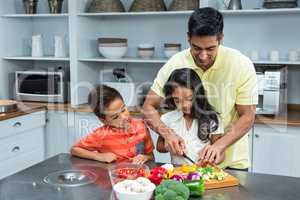 Smiling father slicing vegetables with his children