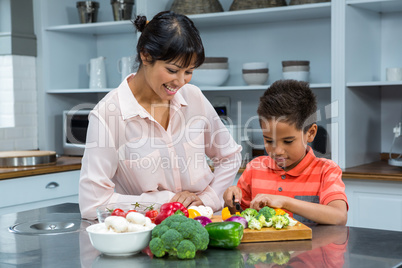 Smiling mother looking at her son slicing vegetables