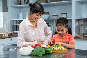 Smiling mother looking at her son slicing vegetables