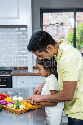 Kind father helping his daughter slicing vegetables