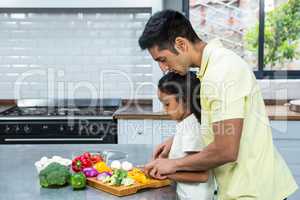 Kind father helping his daughter slicing vegetables