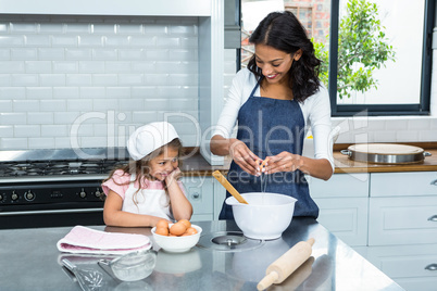 Smiling mother and daughter breaking eggs