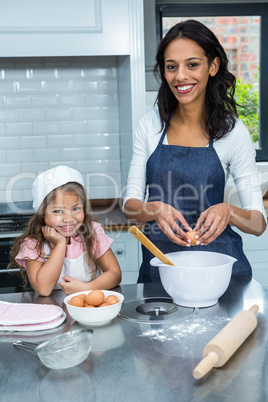 Smiling mother and daughter breaking eggs