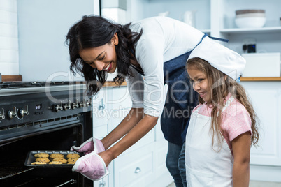 Smiling mother putting biscuits into the oven with daughter