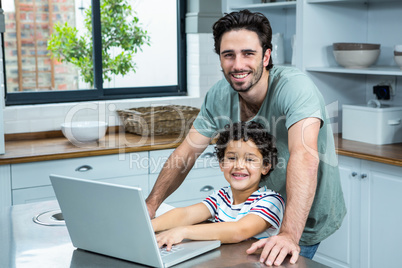 Smiling father using laptop with his son in the kitchen