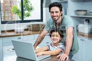 Smiling father using laptop with his son in the kitchen