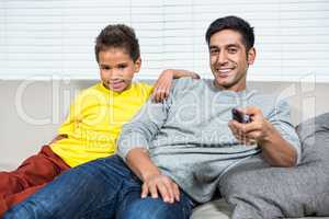 Smiling father and son watching tv on the sofa