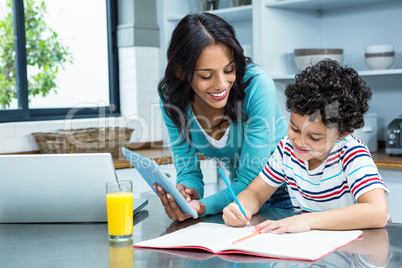 Kind mother helping her son doing homework in kitchen