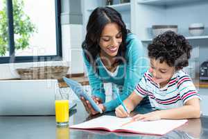 Kind mother helping her son doing homework in kitchen