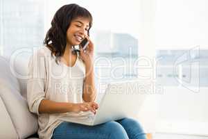 Smiling casual woman having a phone call while using laptop