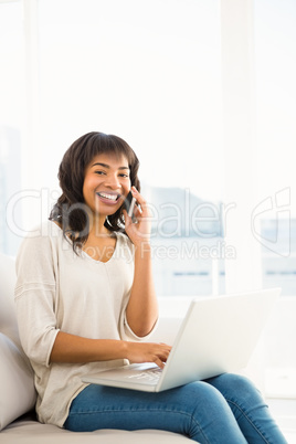 Smiling casual woman having a phone call while using laptop