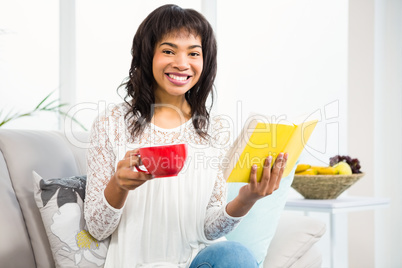 Smiling casual woman holding book and a cup of coffee