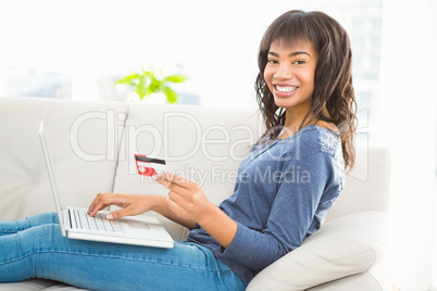 Casual smiling woman using laptop while holding a card