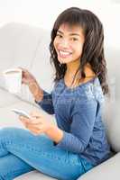 Casual smiling woman holding coffee and smartphone