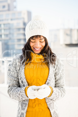 Smiling woman wearing winter clothes and typing on her phone