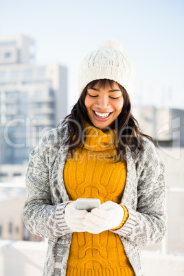 Smiling woman wearing winter clothes and typing on her phone