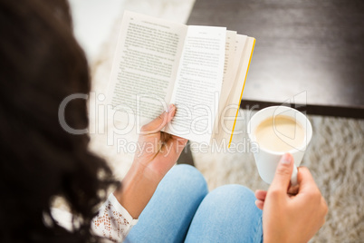 Over shoulder view of woman holding cup of coffee and book