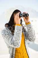 Smiling woman wearing winter clothes and looking into binoculars