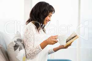 Side view of a woman holding cup of coffee and book
