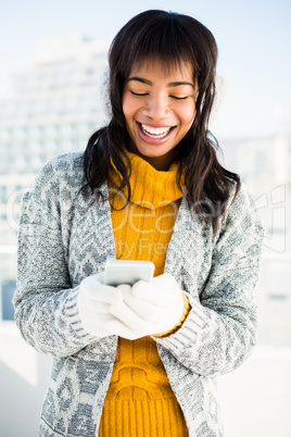 Smiling woman wearing winter clothes and typing on her phone