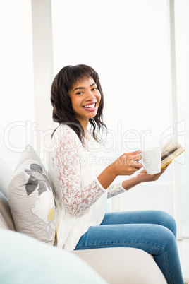 Smiling casual woman holding book and a cup of coffee
