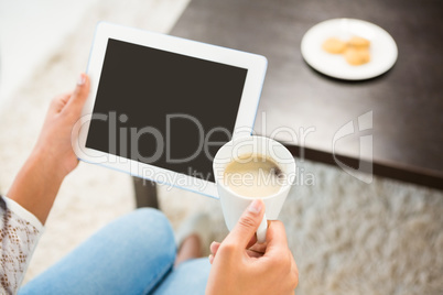 Smiling casual woman using her tablet while holding coffee Smiling casual woman using her tablet while holding coffee