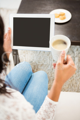 Over shoulder view of casual woman using tablet while holding co