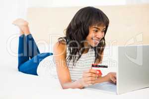 Casual smiling woman using laptop while holding a card