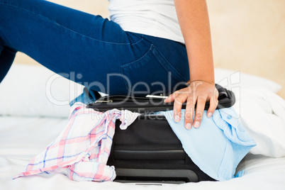 Woman sitting on her overfull suitcase