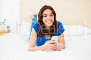 Smiling woman using smartphone while lying on bed