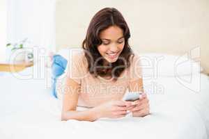 Smiling woman using smartphone while lying on bed