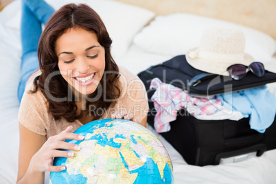 Smiling woman lying on bed while holding a globe