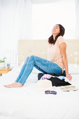 Woman sitting on her overfull suitcase