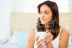 Happy woman holding cup of coffee while sitting on bed