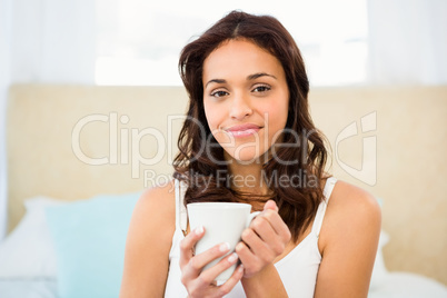 Happy woman holding cup of coffee while sitting on bed