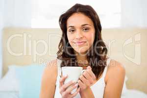 Happy woman holding cup of coffee while sitting on bed