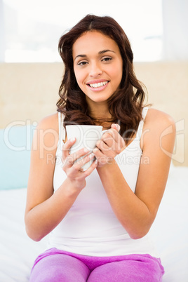 Happy woman holding cup of coffee while sitting on bed