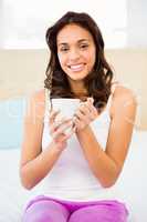 Happy woman holding cup of coffee while sitting on bed