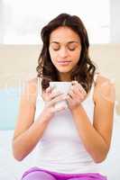 Happy woman holding cup of coffee while sitting on bed