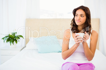 Happy woman holding cup of coffee while sitting on bed